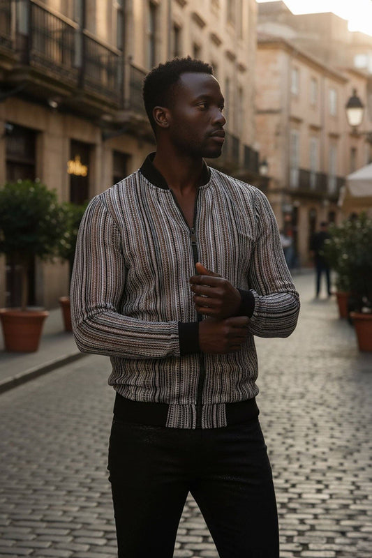 A man wearing a vertically striped zip-up bomber jacket with black trim and black pants, standing on a cobblestone street in an urban European-style setting.