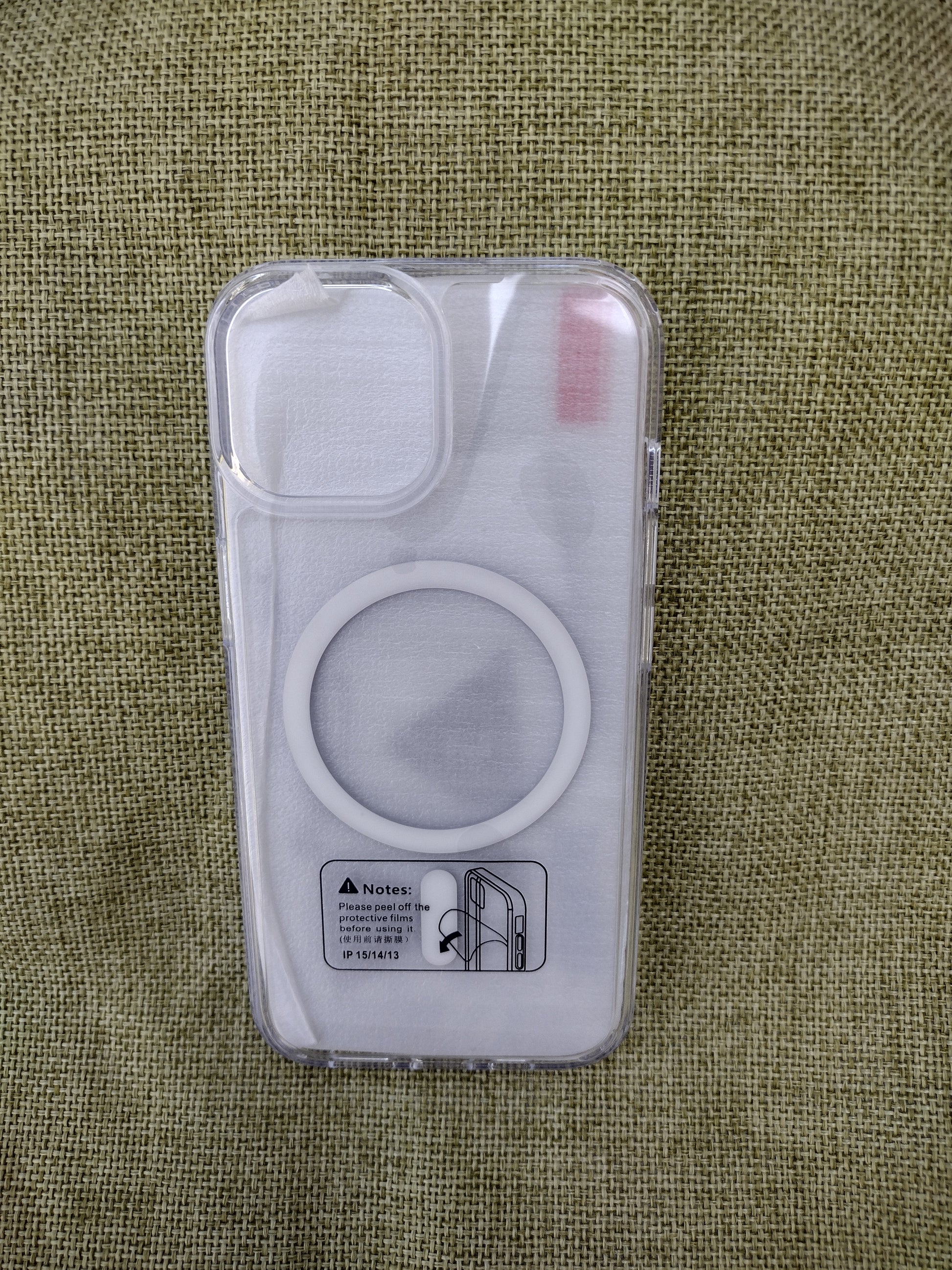 A clear MagSafe-compatible phone case with a white magnetic ring, shown empty on a textured olive green fabric background.